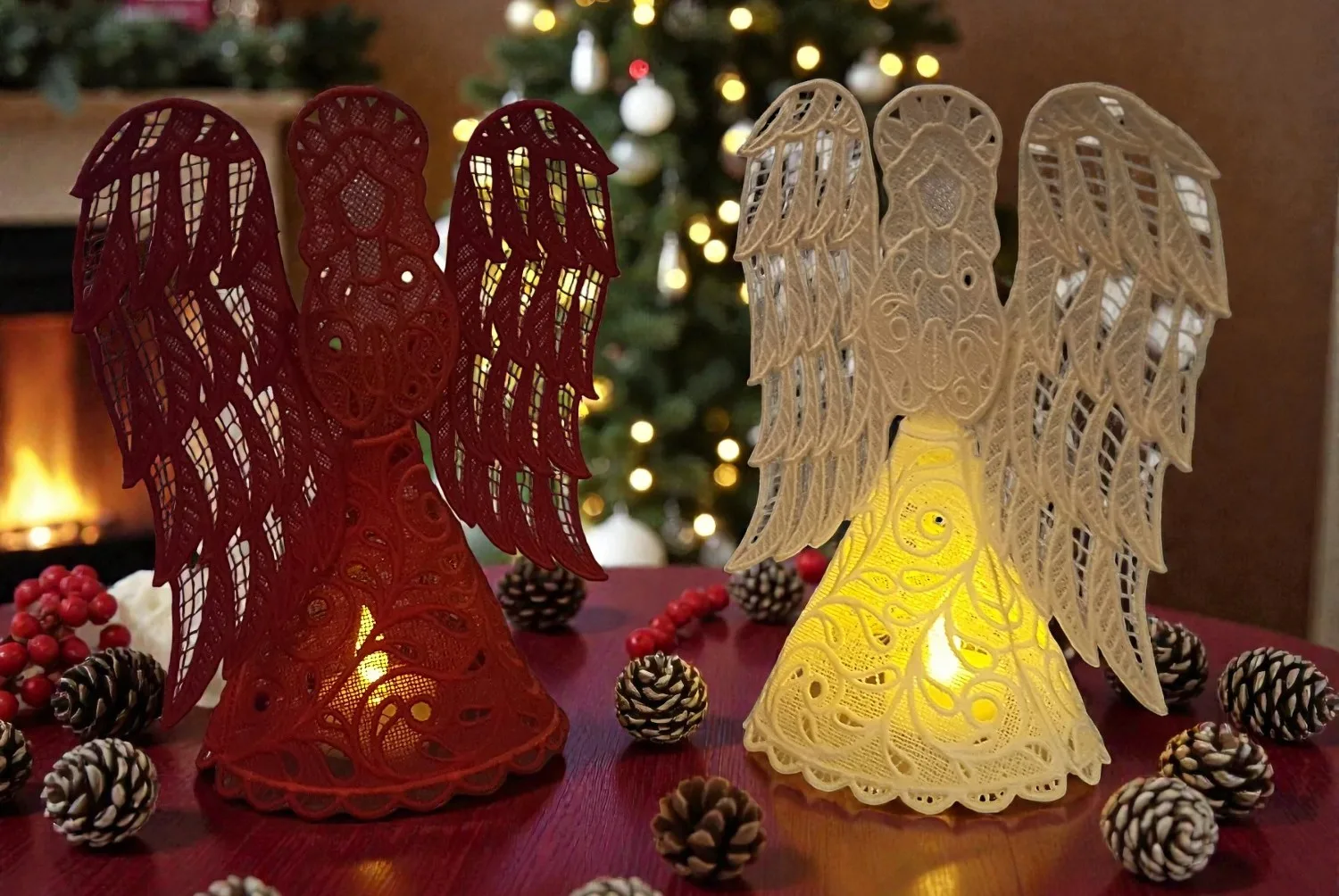 Embroidered angel figures in red and cream with LED lights, surrounded by pine cones and berries on a table.